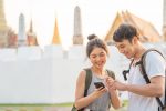 Traveler Asian couple direction on location map in Bangkok, Thailand, sweet couple using mobile phone looking on map while spending holiday trip in sunset. Lifestyle couple travel in city concept.